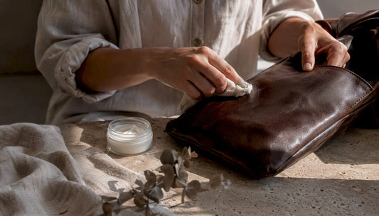 Hands cleaning leather bag with cloth and conditioner